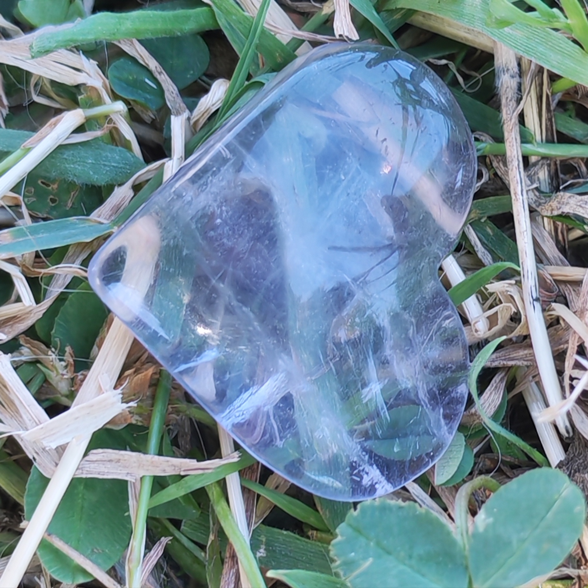 Gros plan sur la fluorite bleue AA montrant les strates internes, les nuances bleues et les zones translucides typiques de cette pierre., dans l herbe