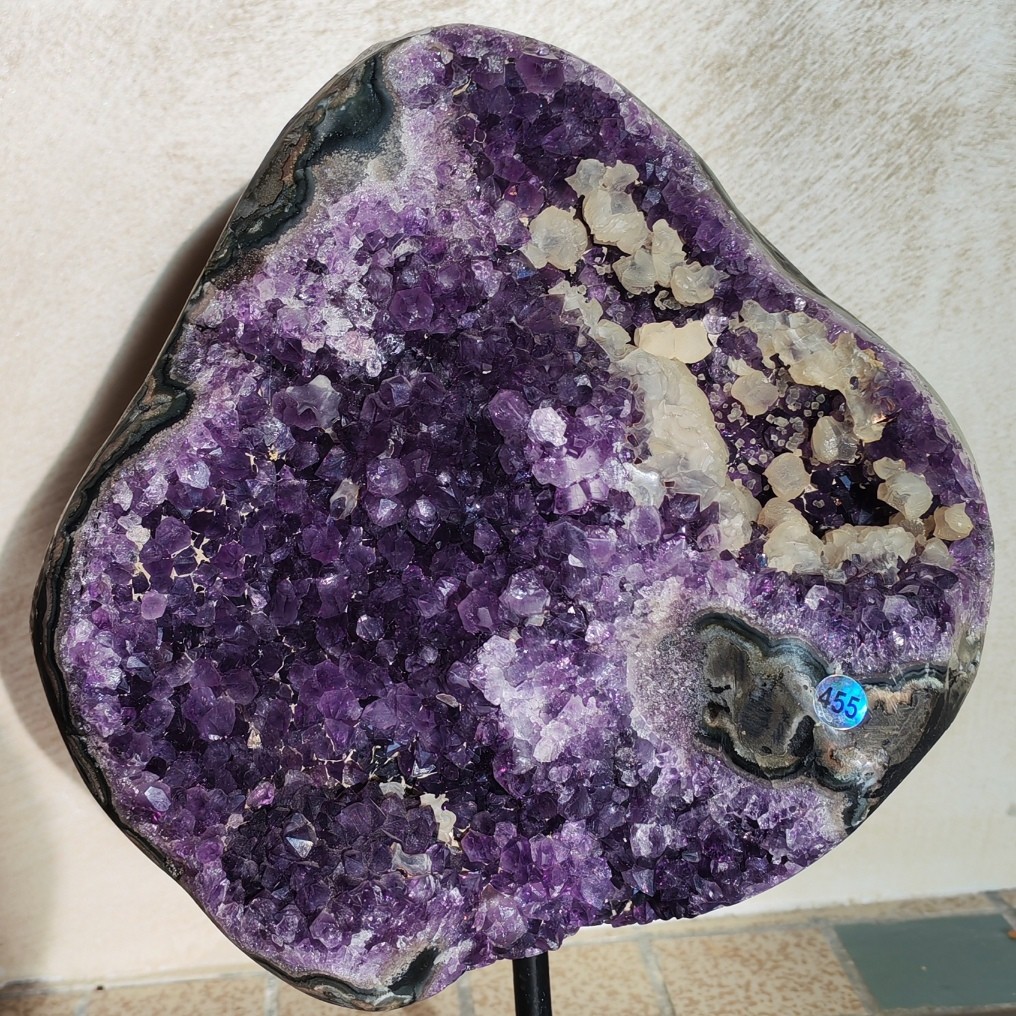 Géode d’améthyste violette sur socle métallique noir, avec cristaux blancs contrastés et pourtour présentant des bandes minérales calcites et pied métal