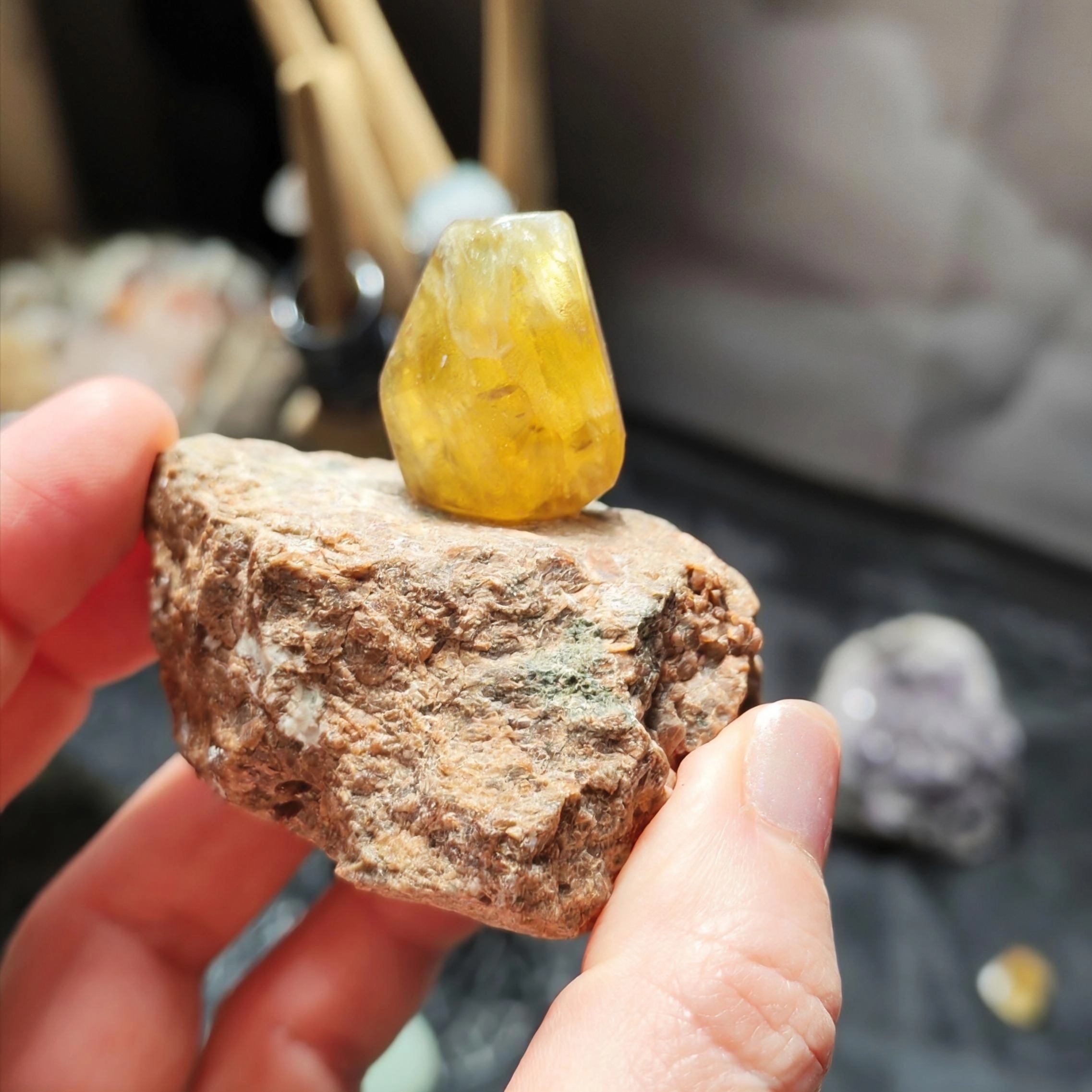 Fluorite jaune translucide sur matrice brute tenue dans une main en intérieur