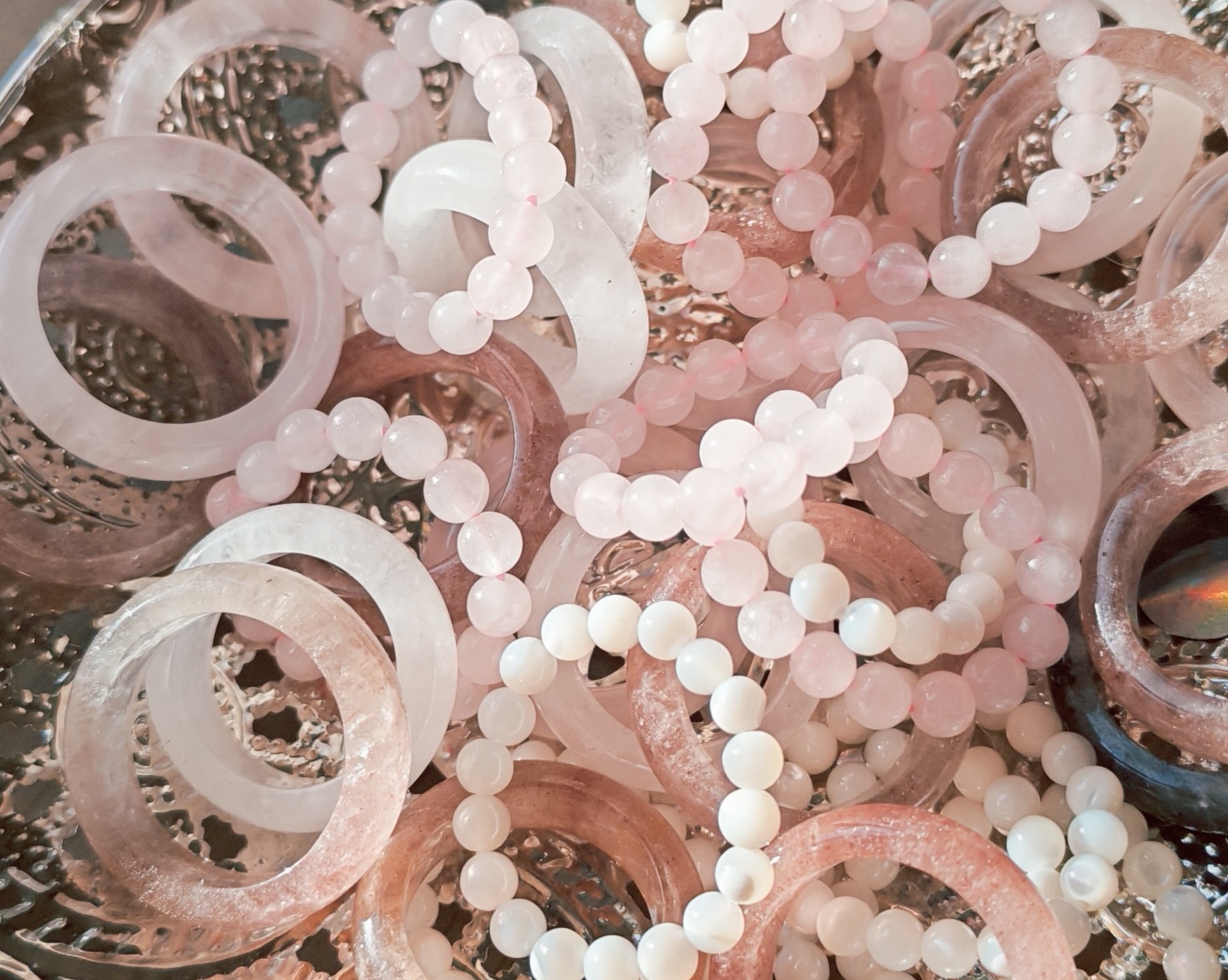 Vue du dessus de bagues joncs roses et translucides et de bagues en perles rondes sur un plateau argenté