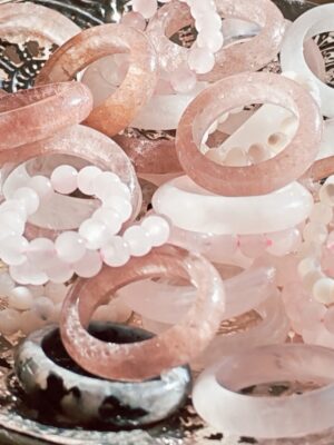 Assortiment de bagues joncs roses et transparentes avec des bagues en perles blanches et roses sur un plateau argenté